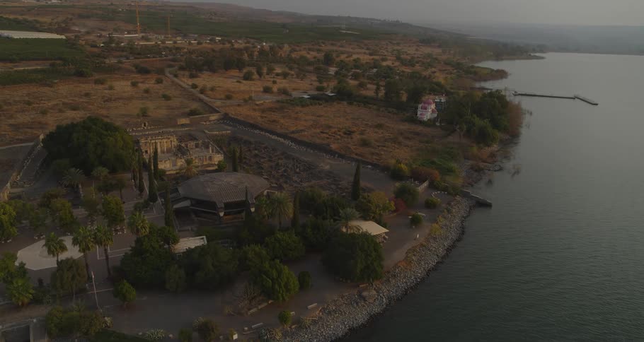 A serene aerial shot pushing in towards the archeological site of Capernaum on the coast of the Sea of Galilee at dawn