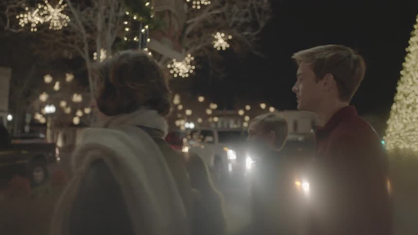 A family walks past a christmas tree in a town at night