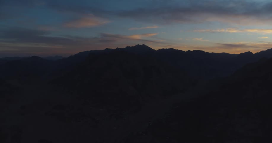 A stunning aerial shot captures the silhouette of a vast mountain range against a colorful dusk sky