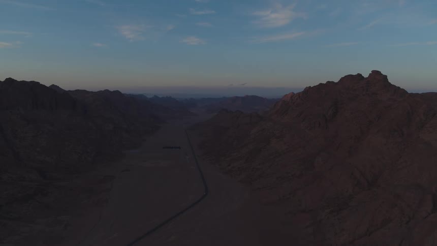 An aerial view of a vast, tranquil desert valley with a long road cutting through the mountains at twilight
