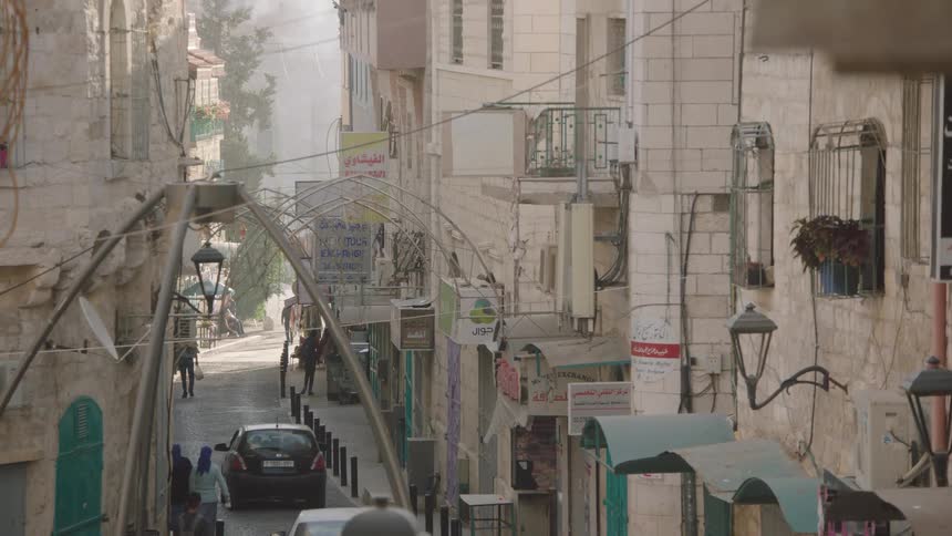 A hazy view looking down a narrow, historic cobblestone street in a Middle Eastern city as pedestrians walk by