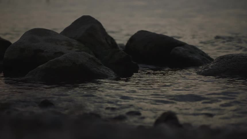 Gentle waves wash over dark rocks on a serene shoreline at dusk