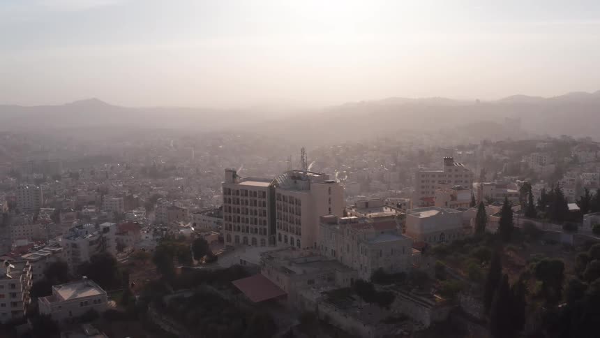 Slow aerial pull-back reveals a vast, hazy city on a hillside during a beautiful sunrise