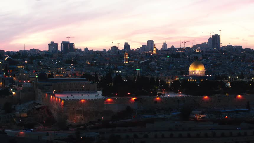 An establishing shot of the illuminated Old City of Jerusalem and the golden Dome of the Rock against a beautiful twilight sky