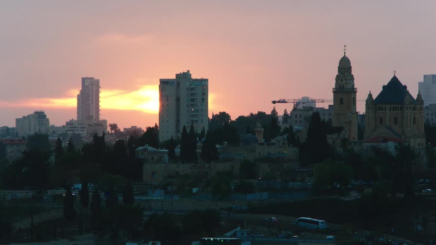 The sun sets behind the modern and ancient skyline of Jerusalem, casting a warm glow over the Abbey of the Dormition