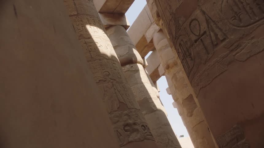 A low-angle view reveals the immense scale and intricate hieroglyphic carvings on the ancient columns of an Egyptian temple