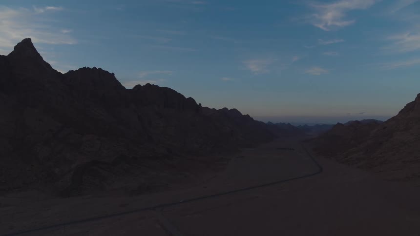 An epic aerial view captures a lone road stretching through a vast desert mountain valley at dusk