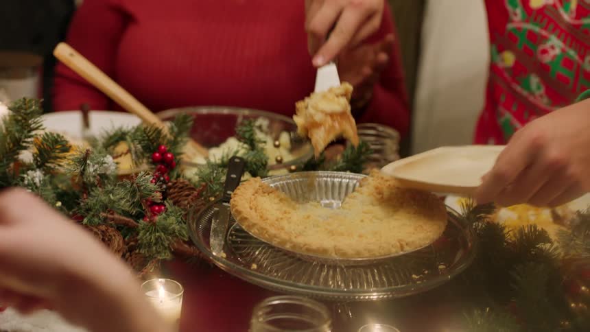 Person cuts a slice of pie out of a tin and hands it to a person