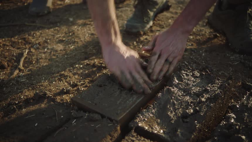 A craftsman carefully packs and smooths wet mud into a rectangular wooden mold to form a traditional adobe brick