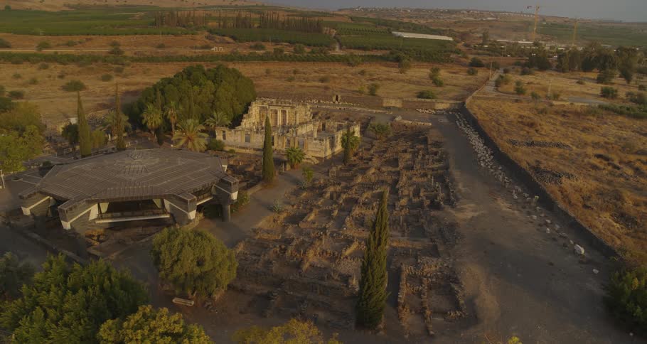 Tilting aerial view reveals the ancient ruins of Capernaum, featuring the synagogue and modern church, basking in the golden light of sunrise