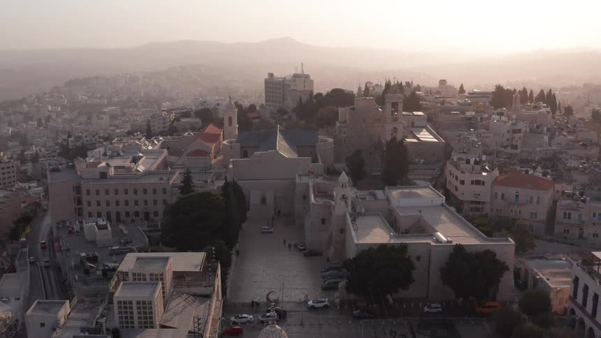 A serene aerial view slowly pulls back from the historic Church of the Nativity in Bethlehem as the sun sets over the city