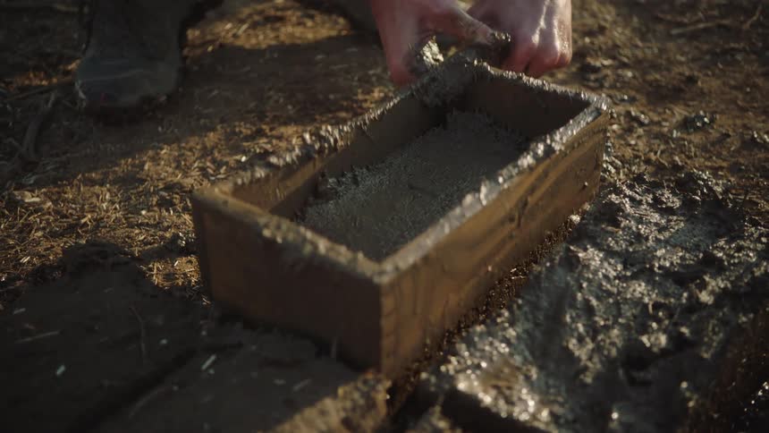 Close up in slow motion of hands molding a wet mud brick using a traditional wooden form