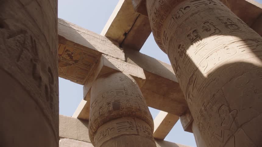A low-angle shot captures the details of massive, carved stone pillars and ceiling beams of an ancient Egyptian temple
