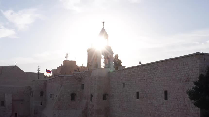 A beautiful aerial shot rises over the iconic Church of the Nativity in Bethlehem as the bright sun sets behind the bell tower