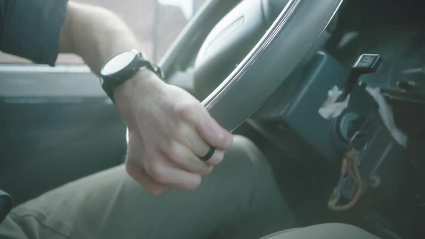 Slow motion close-up of a man's hands on the steering wheel as he drives through a sunny, hazy landscape