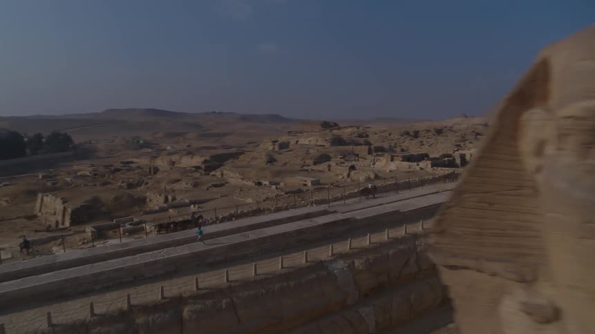 An aerial shot pans from the Great Sphinx to a man running along a path with the majestic Giza Pyramids in the background
