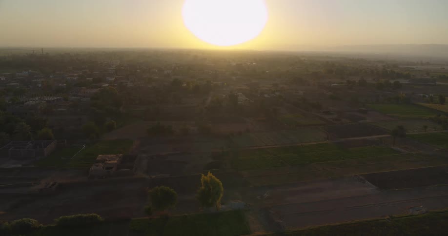 A slow aerial pullback reveals a rural agricultural landscape under a beautiful, hazy sunset