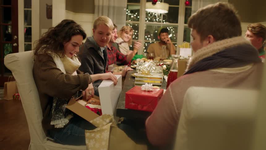 A group of people open presents around a dining room table