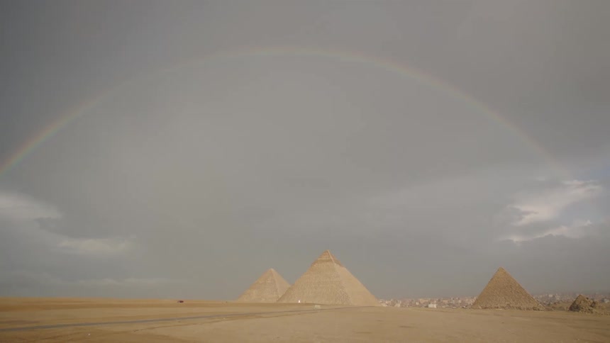 A rare and beautiful rainbow stretches across a dramatic, stormy sky above the Great Pyramids of Giza in the Egyptian desert