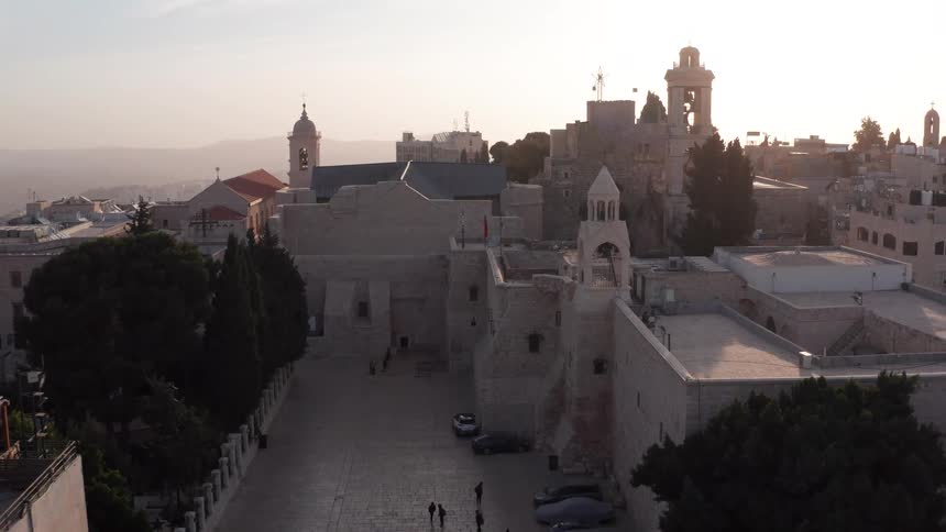 An aerial view pulls back from the historic Church of the Nativity in Bethlehem during a beautiful, hazy sunset