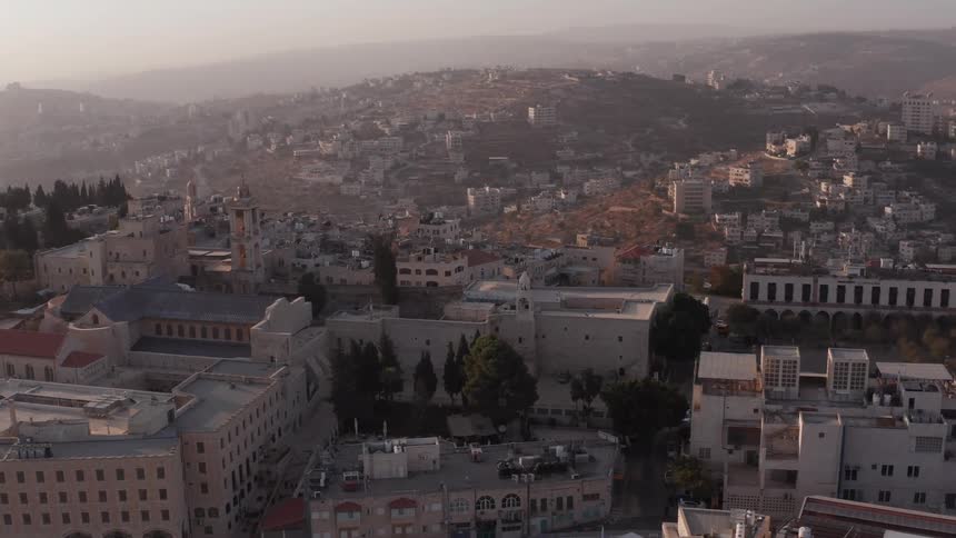 An aerial view of the historic city of Bethlehem at sunrise, showing the Church of the Nativity surrounded by ancient buildings and rolling hills