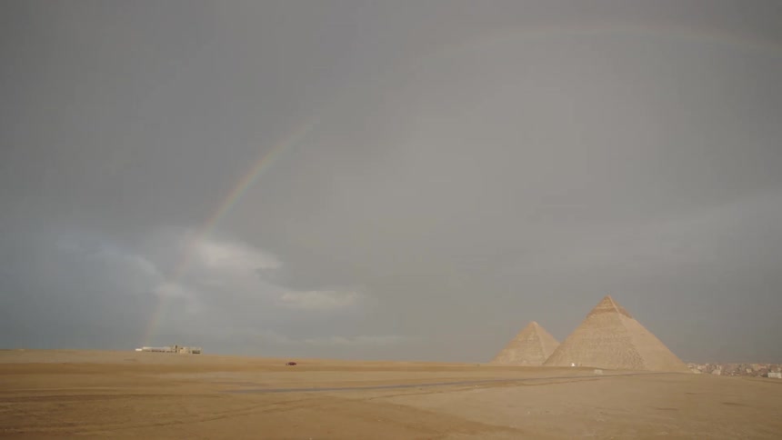 A magnificent rainbow arches over the iconic Pyramids of Giza in the Egyptian desert under a stormy sky