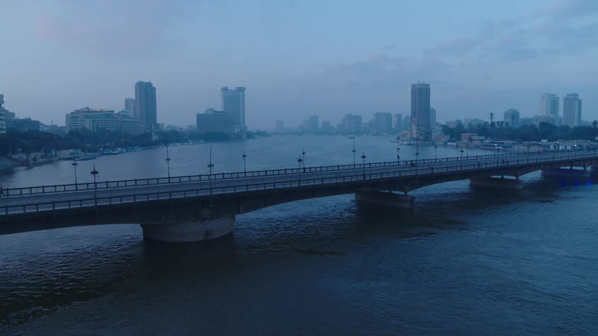 A static wide shot of a bridge crossing the Nile River in Cairo, Egypt during a quiet, hazy blue hour
