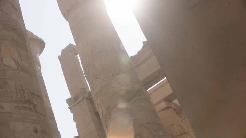 Sunlight streams between the massive hieroglyphic columns of an ancient Egyptian temple