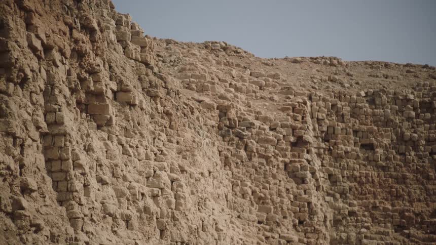 A static low-angle shot of a crumbling ancient ruin wall made of mud bricks in a desert