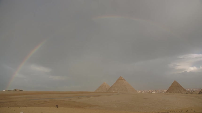 A stunning rainbow appears in the cloudy sky above the ancient Pyramids of Giza in the Egyptian desert