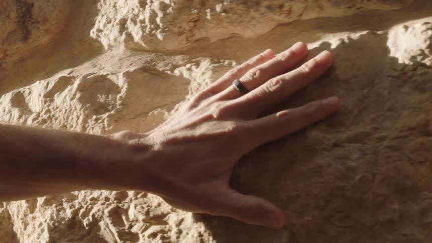 A slow-motion close-up of a person's hand gently sliding across a warm, sunlit stone wall