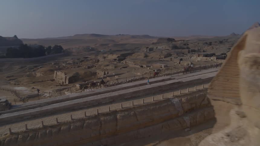 A stunning aerial shot flies past the Great Sphinx, revealing tourists riding camels and the Giza pyramids in the distance