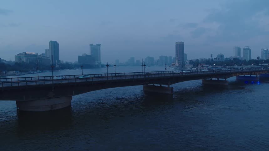 Early morning traffic crosses a bridge over the Nile River with the Cairo city skyline in the background