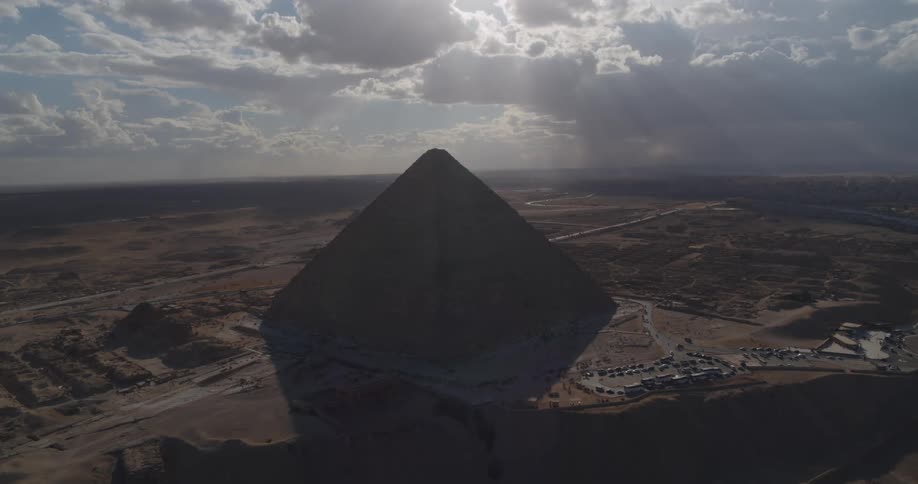 High aerial wide shot of the Great Pyramid of Giza silhouetted against a cloudy sky with powerful sunbeams