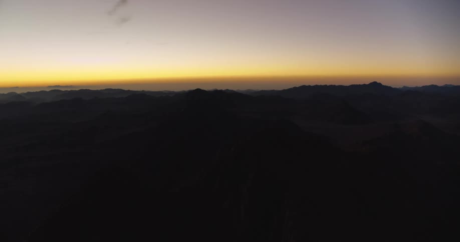 The golden light of dawn breaks over a dark, silhouetted mountain range