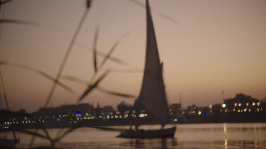 A slow focus pull reveals a traditional Egyptian felucca sailboat gracefully gliding on the Nile River at sunset