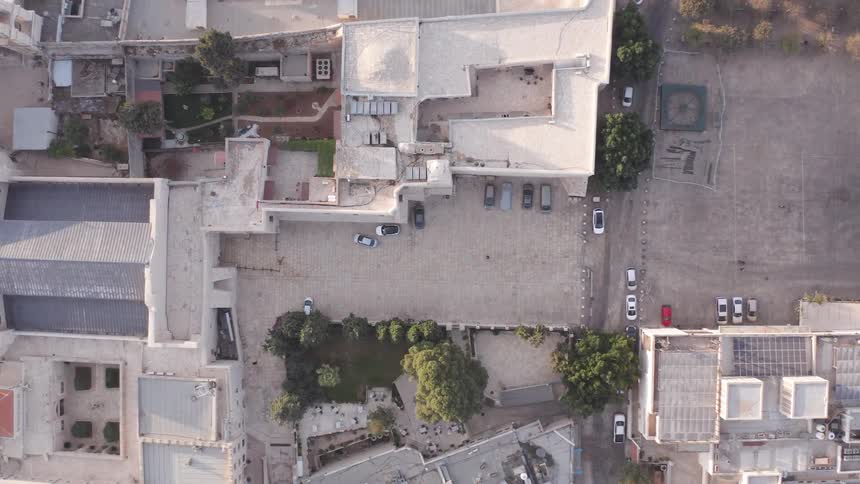 An ascending bird's-eye view reveals the intricate layout of a historic city's stone courtyards and ancient rooftops