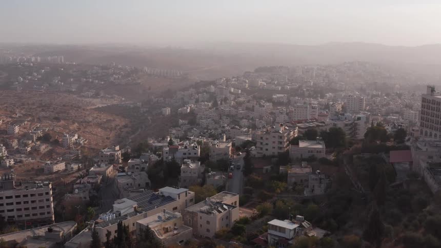 An aerial view flies over a historic church and bell tower, revealing the ancient city of Bethlehem, Israel during a hazy sunrise
