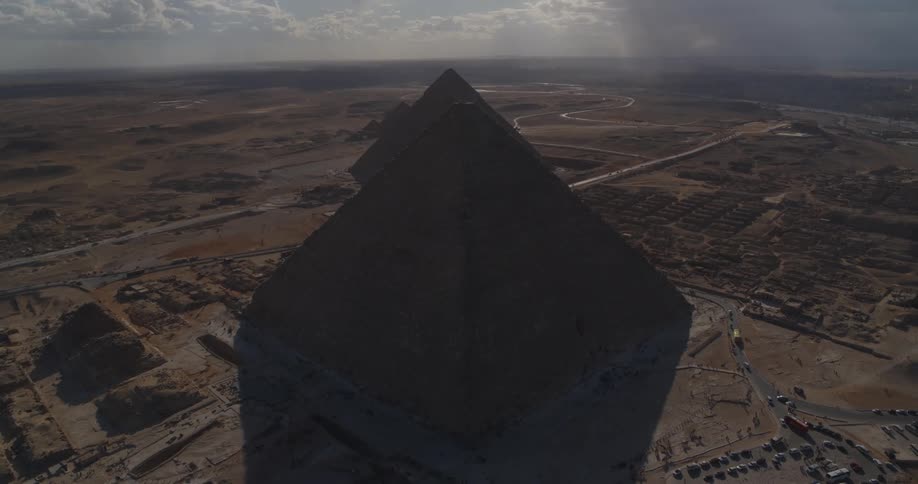 A slow aerial ascent reveals the three iconic Pyramids of Giza silhouetted against the desert landscape at sunset