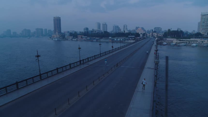 An aerial view follows a lone runner crossing a deserted city bridge over the Nile River in Cairo at dawn