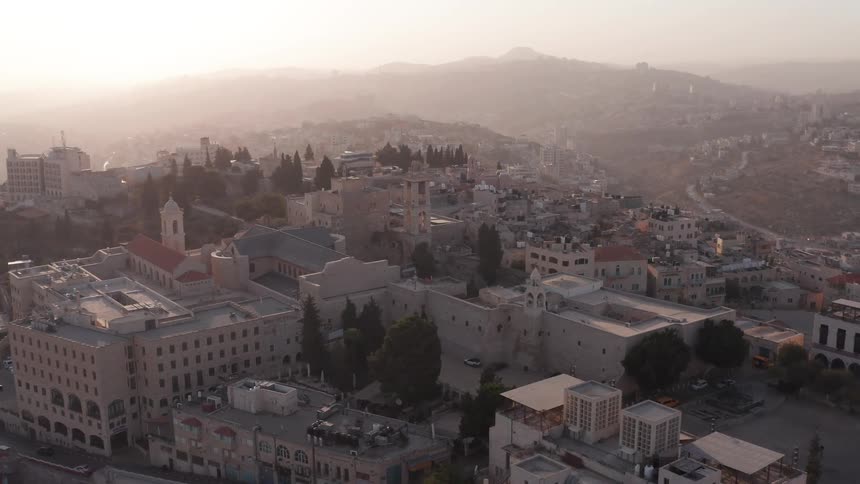 A stunning aerial view reveals the historic Church of the Nativity in Bethlehem, bathed in the soft, hazy light of a golden sunrise