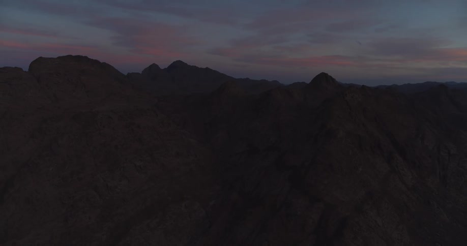A wide shot of a silhouetted, rugged mountain range under a colorful twilight sky