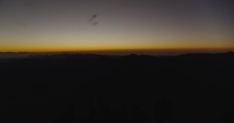 A beautiful golden hour sunrise paints the horizon above a dark, silhouetted mountain range