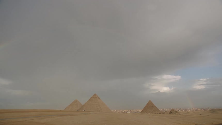 A rare rainbow arches over the ancient Pyramids of Giza under a dramatic, stormy sky