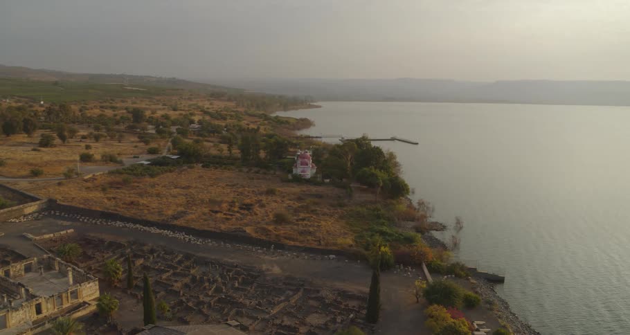 An aerial view pans over the ancient ruins of Capernaum on the shores of the Sea of Galilee during a hazy sunrise