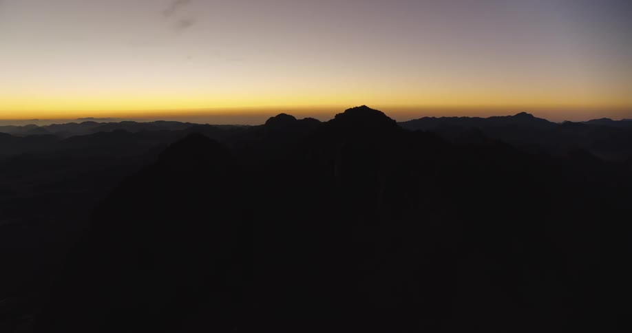 A stunning aerial view reveals the vast, silhouetted mountain range of Mount Sinai against the warm glow of a predawn sky
