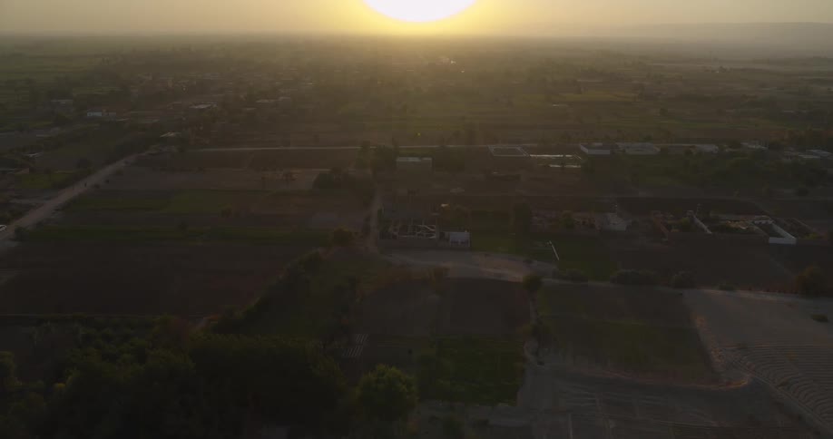 Aerial footage captures a sprawling rural landscape with agricultural fields bathed in the warm light of a hazy sunrise