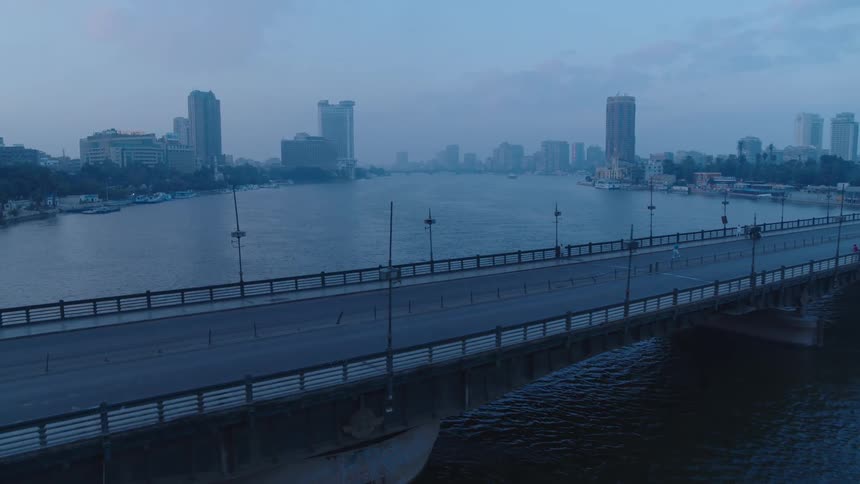 A slow aerial push-in shot reveals the nearly empty 6th of October Bridge over the Nile River against the Cairo skyline at dawn