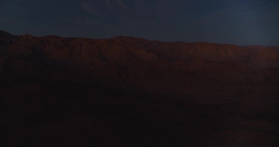 A majestic, dark mountain range stands silhouetted against a deep blue twilight sky