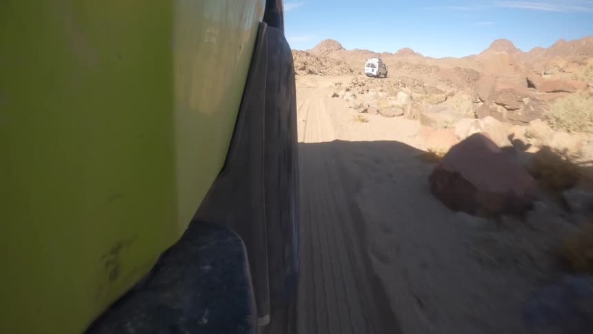 A low-angle POV shot from a green off-road vehicle driving on a rugged and sandy desert trail